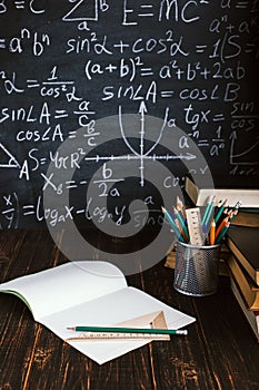 School desk in classroom, with books on background of chalk board with written formulas. Soncept Teacher`s Day