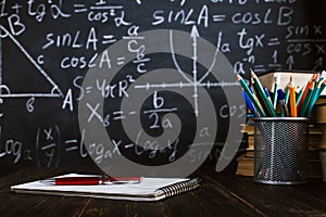 School desk in classroom, with books on background of chalk board with written formulas. Soncept Teacher`s Day