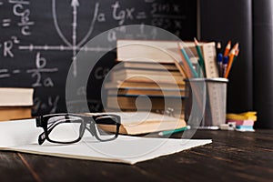 School desk in classroom, with books on background of chalk board with written formulas. Soncept Teacher`s Day