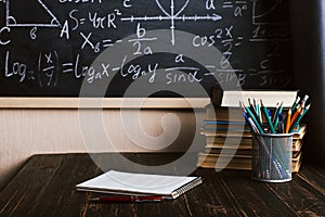 School desk in classroom, with books on background of chalk board with written formulas. Soncept Teacher`s Day