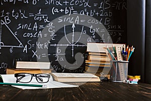 School desk in classroom, with books on background of chalk board with written formulas. Soncept Teacher`s Day