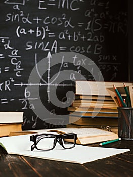 School desk in classroom, with books on background of chalk board with written formulas. Soncept Teacher`s Day