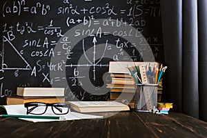 School desk in classroom, with books on background of chalk board with written formulas. Soncept Teacher`s Day