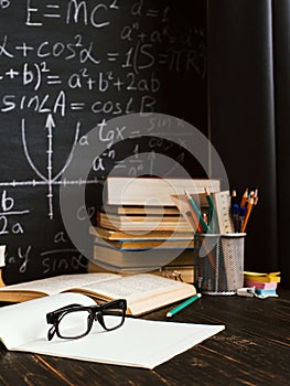 School desk in classroom, with books on background of chalk board with written formulas. Soncept Teacher`s Day