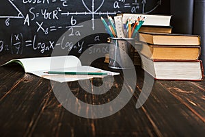 School desk in classroom, with books on background of chalk board with written formulas. Soncept Teacher`s Day. Copy spase