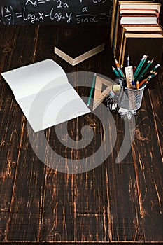 School desk in classroom, with books on background of chalk board with written formulas. Soncept Teacher`s Day. Copy spase