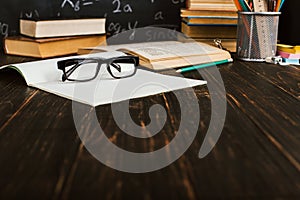 School desk in classroom, with books on background of chalk board with written formulas. Soncept Teacher`s Day. Copy spase