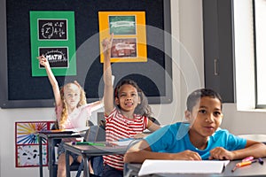 In school, diverse young students raising hands in the classroom, eager to answer photo