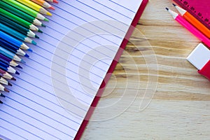 School and drawing supplies, on wooden table. Exercises book, colored pencils, eraser, pencil and ruler.