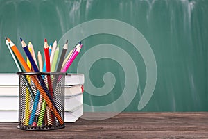 School education concept. Close-up photo of colorful crayons and stack of textbooks isolated on green chalkboard copyspace