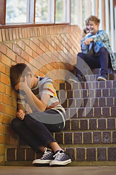 School friend bullying a sad boy in school corridor