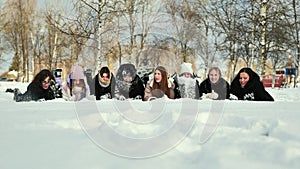School friends lie in the snow and sprinkle snow on each other.