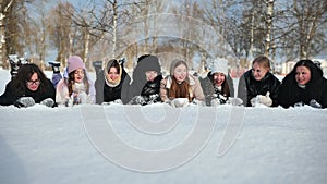 School friends lie in the snow and sprinkle snow on each other.