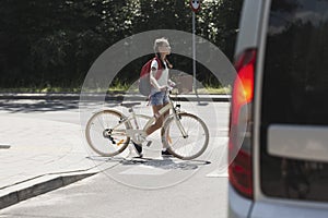 School girl with bike walk in pedestrian crossing in front of a car