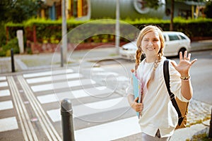 School girl crossing crosswalk and hand waving outdoors in city