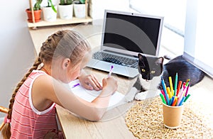 School girl doing homework at home, writing or drawing, cat lying nearby.