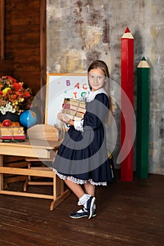 School Girl in dress holds a stack of books. Back to school. Happy smiling Little girl with books stand near of chalkboard.