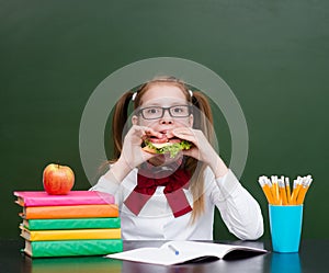 School girl eating sandwich near empty green chalkboard