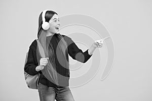 School girl in headphones with backpack ready to learn. School children with school bag on isolated yellow studio