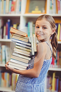 School girl holding stack of books in library