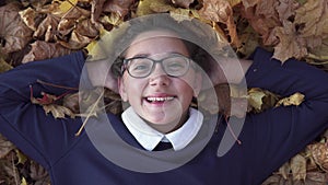 School girl lies on autumn leaves and smiling at park