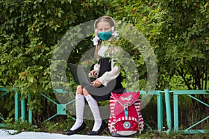 School girl in a medical mask, headphones engaged in a park on a laptop. Back to school. Virus protection for schools.