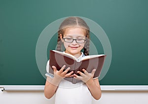 School girl read book, posing at school board, empty space, education concept