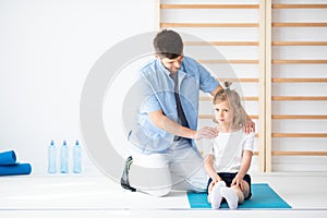 School girl sitting on blue yoga mat talking to her handsome young physician