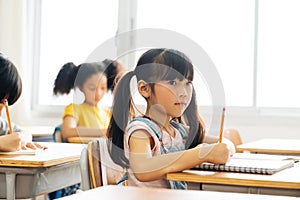 School girl sitting in school writing in book with pencil, studying, education, learning. Asian children in the class