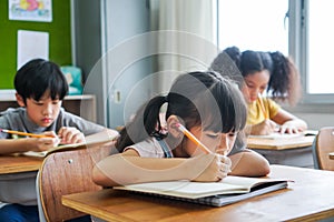 School girl sitting in school writing in book with pencil, studying, education, learning. Asian children in the class