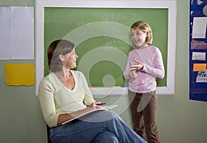 School girl and teacher by blackboard in classroom