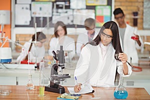 School girl writing in journal book while experimenting in laboratory