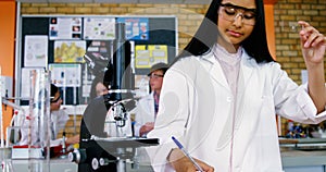 School girl writing in journal book while experimenting in laboratory