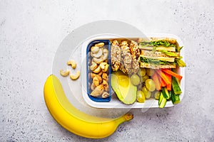 School healthy lunch box with sandwich, cookies, fruits and avocado on white background