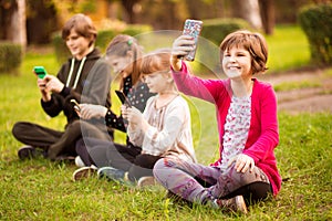 School holidays. Happy child girl take selfie on phone with group of happy friends outdoors in park