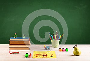 School items on desk with empty chalkboard