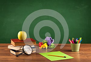 School items on desk with empty chalkboard