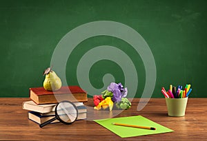 School items on desk with empty chalkboard