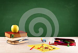 School items on desk with empty chalkboard