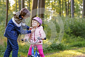 School kid boy, brother put on little preschool sister girl bike helmet on head. Brother teaching happy child cycling