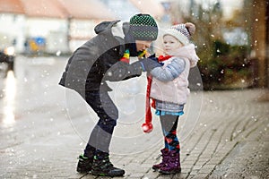 School kid boy and brother warming hands of little sister, toddler girl on cold snowy grey winter day. Family, two