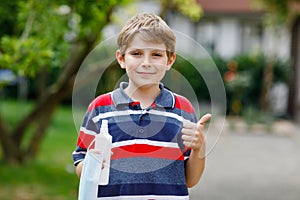 School kid boy with medical mask as protection against pandemic coronavirus quarantine disease. Child holding bottle