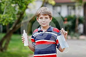 School kid boy with medical mask as protection against pandemic coronavirus quarantine disease. Child holding bottle