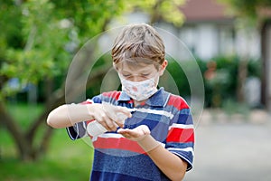 School kid boy with medical mask as protection against pandemic coronavirus quarantine disease. Child holding bottle