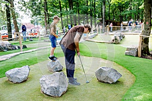 School kid boy playing mini golf with father. Happy child and dad, young man having fun with outdoor activity. Summer