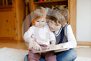 School kid boy reading book for little toddler baby girl, Two siblings sitting together and read books. Beautiful lovely