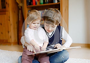 School kid boy reading book for little toddler baby girl, Two siblings sitting together and read books. Beautiful lovely