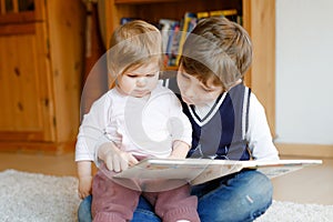 School kid boy reading book for little toddler baby girl, Two siblings sitting together and read books. Beautiful lovely