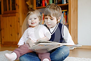 School kid boy reading book for little toddler baby girl, Two siblings sitting together and read books. Beautiful lovely