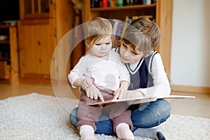 School kid boy reading book for little toddler baby girl, Two siblings sitting together and read books. Beautiful lovely